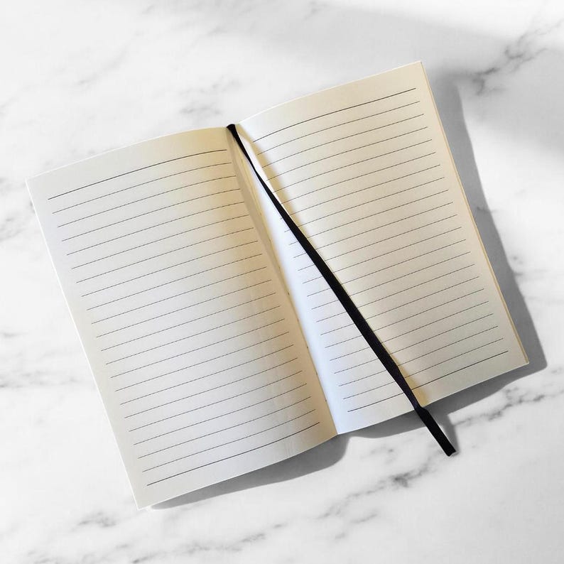 May include: A blank lined notebook with a black ribbon bookmark. The notebook is open to a blank page.