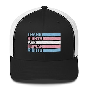 May include: Black and white trucker hat with a black front panel and a white mesh back panel. The front panel features a transgender pride flag and the text "Trans Rights Are Human Rights".