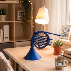 Può includere: Una lampada da scrivania blu brillante a forma di corno, dotata di una base ampia a campana, un corpo circolare avvolto e tre tasti valvola. La lampada presenta un collo lungo e sottile che si estende dalla struttura, con una finitura opaca.