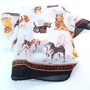 May include: A white lightweight scarf featuring a repeating pattern of various dog breeds in shades of brown, black, and white. The scarf is finished with a dark brown and black border decorated with a repeating bone-shaped graphic print.