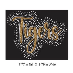 Puede incluir: Un fondo negro con la palabra "Tigers" en purpurina dorada, delineada con pequeños brillantes blancos. El diseño mide 19,7 cm de alto y 24,87 cm de ancho.
