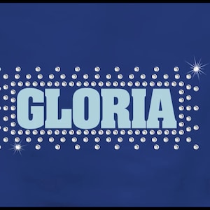 May include: A navy blue background featuring the name "GLORIA" in light blue, embellished with sparkling silver rhinestones. Two starbursts add extra sparkle. The text is in a bold, sans-serif font.