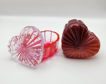 May include: A heart-shaped trinket box with a clear lid and a red base. The lid has a pink and white swirl design. The base has a red and pink swirl design.