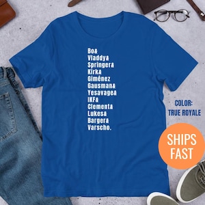 Puede incluir: Una camiseta azul real con texto blanco que enumera nombres. El texto incluye las palabras "Bo", "Vladdy", "Springer", "Kirk", "Giménez", "Gausman", "Yesavage", "IKF", "Clement", "Lukes", "Barger" y "Varscho". La camiseta también tiene el texto "COLOR: TRUE ROYALE".