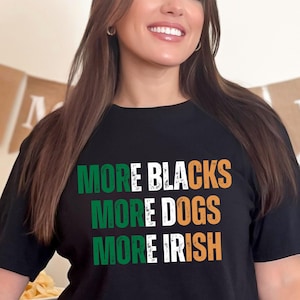May include: Black t-shirt with the text "MORE BLACKS MORE DOGS MORE IRISH" in green, white, and orange. The shirt is a crew neck style and is being worn by a person.