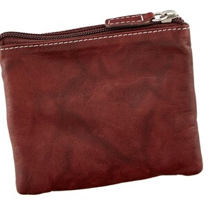 May include: A small, rectangular, burgundy leather coin purse with a silver zipper and white stitching. The purse has a textured surface and a simple, classic design. The zipper pull is also silver.