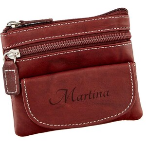 May include: A burgundy leather coin purse with white stitching and silver zippers. The purse has a small front pocket with the name "Martina" printed on it.