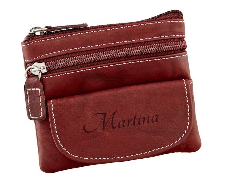 May include: A burgundy leather coin purse with white stitching and silver zippers. The purse has a small front pocket with the name "Martina" printed on it.