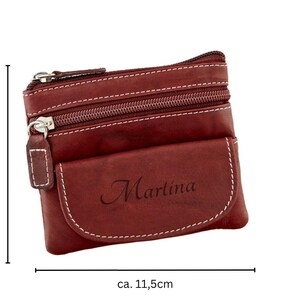 May include: A burgundy leather coin purse with white stitching and two zippered compartments. The purse has a front pocket with the name "Martina" printed on it. The purse is approximately 4 inches tall and 4.5 inches wide.