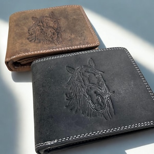 Könnte beinhalten: Zwei Ledergeldbörsen, eine braune und eine schwarze, jeweils mit einem geprägten Pferdekopf-Design. Die Geldbörsen haben weiße Nähte an den Rändern und ein zweifach gefaltetes Design. Die braune Geldbörse liegt oben, leicht angewinkelt.