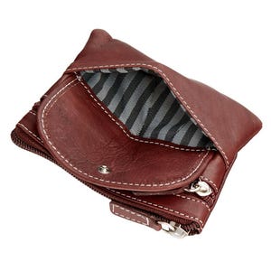 May include: A burgundy leather wallet with white stitching and a striped interior. The wallet has a zippered compartment and a snap closure. The open design reveals the interior lining.
