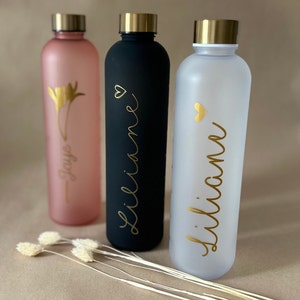 May include: Three water bottles in pink, black, and white, each with a gold lid. The pink bottle has a gold floral design and the name "Jaye". The black and white bottles have the name "Liliane" in gold script.
