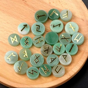 May include: A set of 25 green stone runes with gold lettering. Each rune is a different symbol from the Elder Futhark.