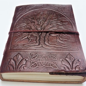 May include: A brown leather journal with a tree of life design embossed on the cover. The cover also features a Celtic knot design and a leather strap closure.