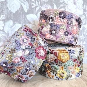 Könnte beinhalten: Drei Rollen florales, gesticktes Tüllband in den Farben Rosa, Grau und Beige. Das Band ist zart und zeigt verschiedene Blumenmuster.