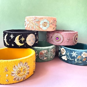 Könnte beinhalten: Eine Auswahl an bestickten Samtbändern in Gelb, Schwarz, Rosa und Türkis. Jedes Armband zeigt einzigartige Himmels- oder Blumendesigns, verziert mit Perlen und Pailletten.