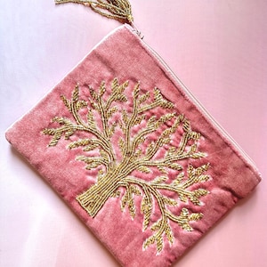 Könnte beinhalten: Rosa Samt-Clutch mit einem goldperlenbesetzten Baumdesign. Die Clutch hat einen Reißverschluss und eine goldperlenbesetzte Quaste. Die Tasche hat eine weiche rosa Farbe und eine rechteckige Form.