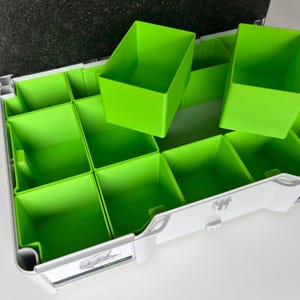 Op de afbeelding: Een witte plastic opbergdoos met meerdere vakken. De vakken zijn bekleed met felgroene, verwijderbare inzetstukken. De doos heeft een label met de tekst "Custom Printery Berlin".