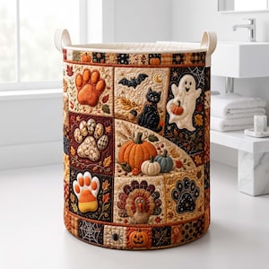 May include: A cylindrical fabric laundry hamper featuring a quilted patchwork design with seasonal autumn and Halloween motifs including pumpkins, a black cat, a ghost, a turkey, and various animal paw prints in shades of orange, brown, and black.