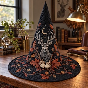 May include: A black quilted witch hat featuring an embroidered stag head centred below a crescent moon. The design includes intricate stitching of orange and brown oak leaves and acorns wrapping around the base and extending up the cone.