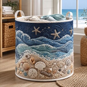 Könnte beinhalten: Ein zylindrischer Aufbewahrungskorb aus Stoff mit einem gesteppten Design einer Meereslandschaft. Die Außenseite zeigt einen Sandstrand mit verschiedenen Muscheln und Seesternen an der Basis, die in blaue Meereswellen und einen Sternenhimmel übergehen.