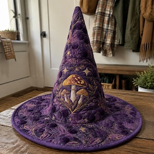 May include: A conical hat in deep purple fabric featuring intricate quilted patterns of mushrooms, leaves, and stars. The design includes a central cluster of three mushrooms in shades of gold and brown, surrounded by detailed stitching and circular motifs.