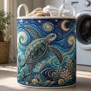 May include: A cylindrical laundry hamper featuring a vibrant blue and gold artistic print of a sea turtle swimming amidst swirling ocean currents, stars, and coral reefs. The hamper has two cream-coloured fabric handles and contains folded fabric.