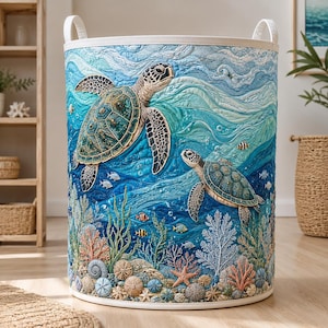 Puede incluir: Un cesto de ropa cilíndrico de tela con una escena oceánica acolchada que muestra dos tortugas marinas nadando entre corales, estrellas de mar y peces pequeños. El diseño utiliza tonos azules y turquesas con asas blancas en el borde.