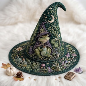 May include: A dark green quilted witch hat featuring an embroidered frog wearing a purple cloak and hat, holding a small bottle. The hat is decorated with botanical patterns, stars, a crescent moon, and small glass bottles attached to the brim.