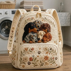 Può includere: Uno zaino trapuntato color crema con un ricamo raffigurante cinque bassotti addormentati dal manto di vari colori. La borsa è decorata con motivi floreali e piccole impronte di zampe, e presenta cerniere dorate e spallacci regolabili.