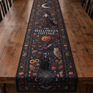 May include: A dark blue quilted table runner featuring a printed design of a witch, a crescent moon, a pumpkin, a witch hat, an owl, a black cat, and a spider web. The text THE HALLOWEEN COTTAGE is printed in the center with autumn foliage.