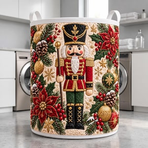 May include: A cylindrical laundry hamper featuring a quilted texture with a central nutcracker figure in a red and green uniform. The design includes festive holiday elements like poinsettias, pinecones, gold ornaments, and holly berries.
