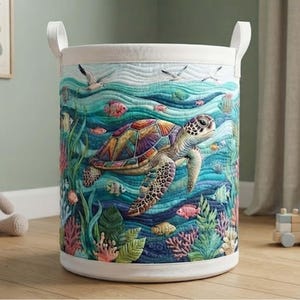 Könnte beinhalten: Ein zylindrischer Wäschekorb mit gesteppter Außenseite und einer lebendigen Unterwasserszene. Das Design zeigt eine große Meeresschildkröte, die zwischen farbenfrohen Korallen, Seetang und verschiedenen kleinen Fischen in Blau-, Grün- und Rosatönen schwimmt.