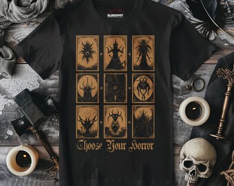 May include: Black t-shirt with a graphic of nine cards featuring different monsters. The cards are arranged in a 3x3 grid. The text "Choose Your Horror" is printed below the cards.