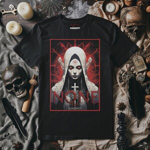 May include: Black t-shirt with a red and white graphic of a woman in a white hooded robe with a cross. The text "NONE" is written in white letters with red outlines. The text "BLINDSPOT" is written in white letters below the graphic.