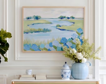 May include: A light green and white cabinet with gold accents and wooden legs. The cabinet is topped with a marble surface, and decorated with a blue vase, a blue and white jar, and a stack of books. A landscape painting hangs above the cabinet.