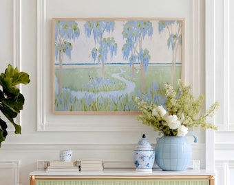 May include: A light green and white cabinet with gold accents and wooden legs. A framed landscape painting hangs above the cabinet. A blue vase and a blue and white patterned jar sit on top of the cabinet, along with a stack of books.