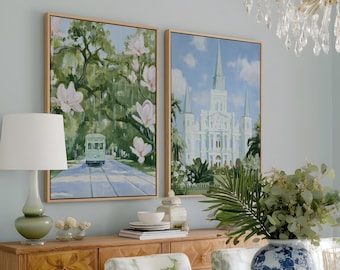 May include: Two framed rectangular wall art prints featuring New Orleans scenes, one depicting a streetcar under oak trees with magnolia blossoms and the other showing St. Louis Cathedral, both displayed above a wooden sideboard with drawers.
