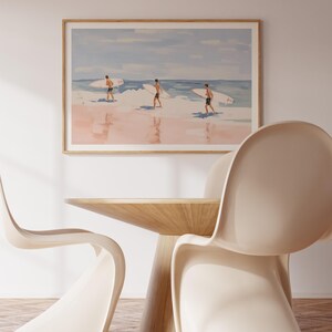 May include: A framed watercolor painting of three people walking on a beach with surfboards. The painting has a light blue sky and pink sand.