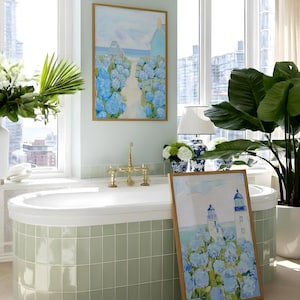 May include: A bathroom scene featuring a white bathtub with brass fixtures, a large framed painting of blue hydrangeas, and a potted plant. The walls are a light green, and the room has large windows.