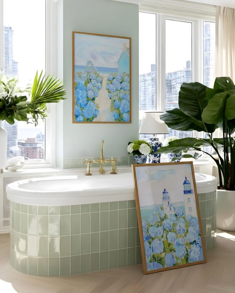 May include: A bathroom scene featuring a white bathtub with brass fixtures, a large framed painting of blue hydrangeas, and a potted plant. The walls are a light green, and the room has large windows.