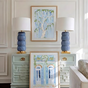 Puede incluir: Dos l&aacute;mparas de cer&aacute;mica azul con pantallas blancas se asientan sobre gabinetes azul claro a juego. Una pintura en acuarela enmarcada de un &aacute;rbol cuelga entre las l&aacute;mparas. Otra pintura enmarcada de un edificio con contraventanas azules est&aacute; al frente.