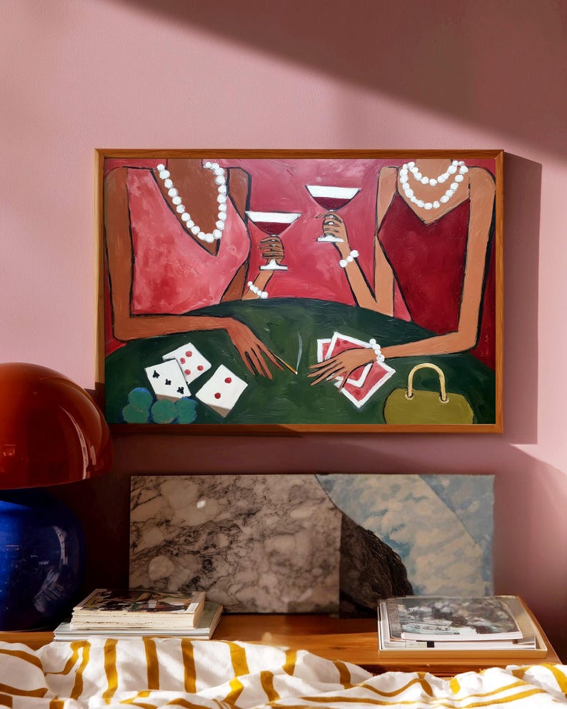 May include: An abstract painting depicts two figures in dresses, playing cards and drinking cocktails. The figures are adorned with pearl necklaces and bracelets. The painting is framed in a wooden frame and hangs on a pink wall. A green table is in the foreground.