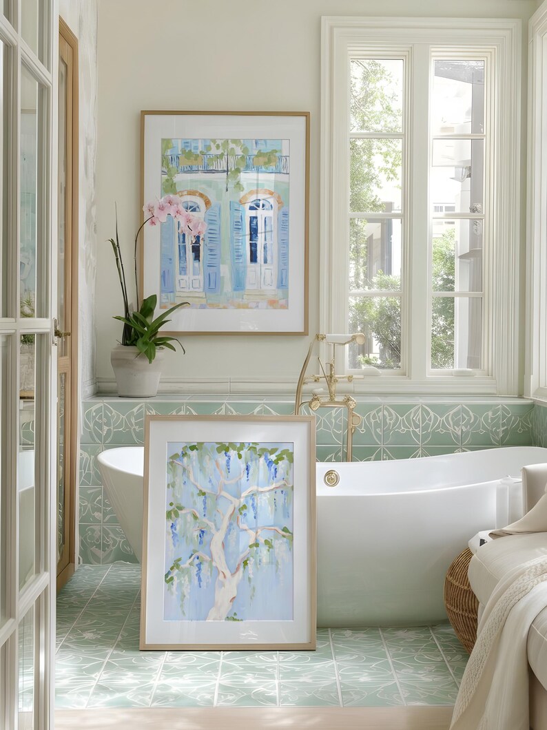 Puede incluir: Dos pinturas de acuarela enmarcadas en un ba&ntilde;o. Una representa un edificio con contraventanas azules, la otra un &aacute;rbol con flores azules. El ba&ntilde;o tiene una ba&ntilde;era blanca, baldosas verdes y una ventana.