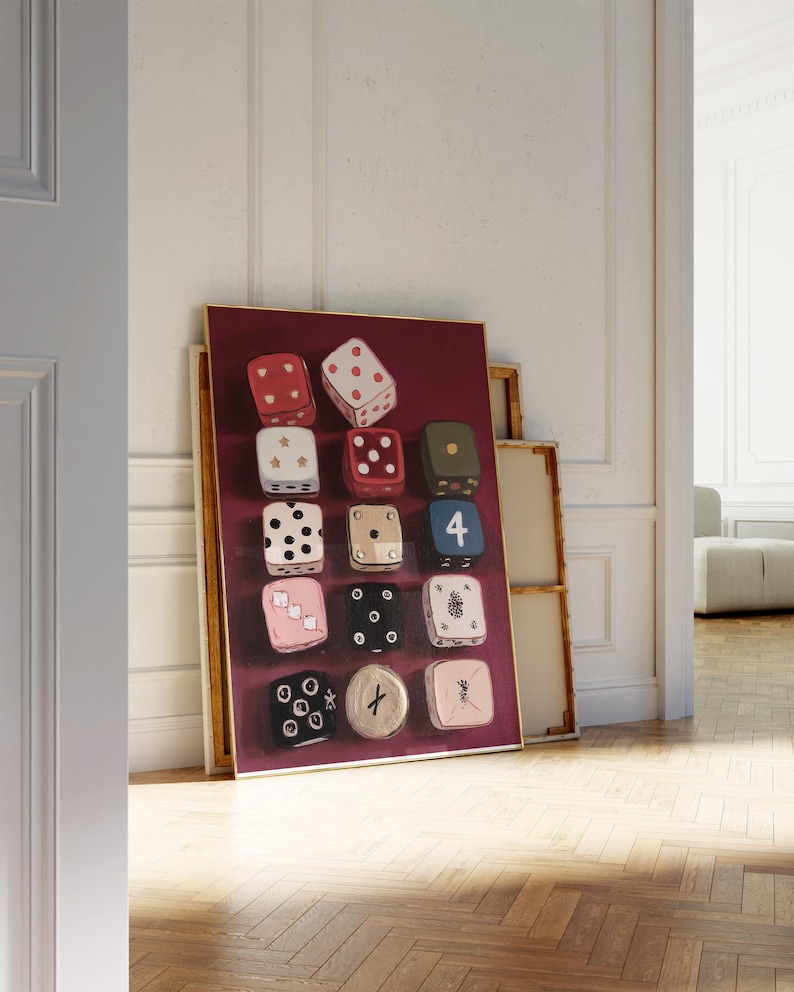 Op de afbeelding: Een ingelijst kunstwerk met twaalf dobbelstenen met diverse ontwerpen en kleuren, tegen een dieprode achtergrond. De dobbelstenen bevatten stippen, sterren en andere symbolen. Het kunstwerk leunt tegen een muur.