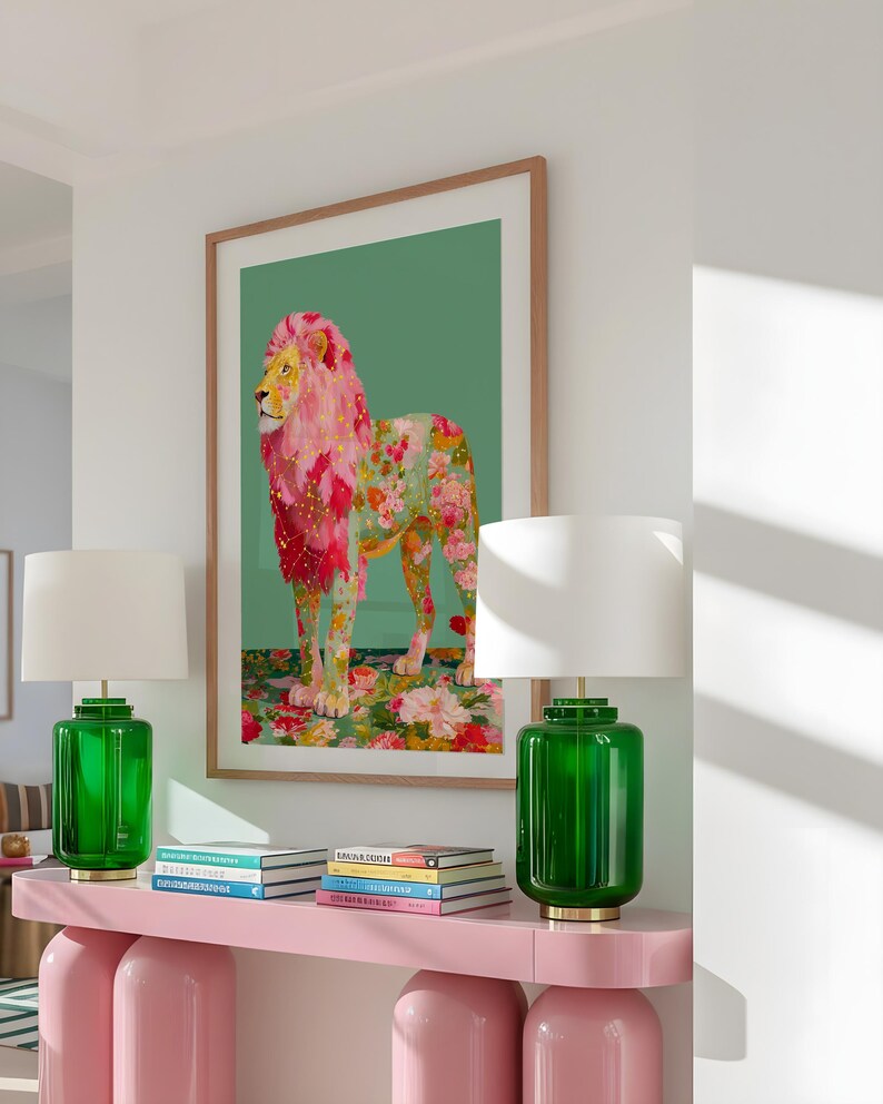 K&ouml;nnte beinhalten: Ein gerahmter Kunstdruck eines L&ouml;wen mit rosa und floraler M&auml;hne und K&ouml;rper, vor einem gr&uuml;nen Hintergrund. Das Kunstwerk wird &uuml;ber einem rosa Konsolentisch mit zwei gr&uuml;nen Glaslampen mit wei&szlig;en Schirmen ausgestellt. B&uuml;cher sind auf dem Tisch gestapelt.