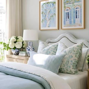 Puede incluir: Un dormitorio con una cama con ropa de cama azul claro y cojines estampados. Dos pinturas de acuarela enmarcadas cuelgan sobre la cama. Un jarr&oacute;n azul y blanco exhibe flores blancas.
