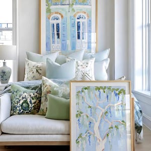 Puede incluir: Una escena interior luminosa con obras de arte enmarcadas y cojines decorativos. Las obras de arte incluyen una pintura de un &aacute;rbol con flores azules y una pintura de contraventanas azules. Los cojines son en tonos azules y verdes.