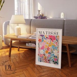 May include: A white framed print of a colorful floral painting by Henri Matisse. The print features a variety of flowers in shades of pink, red, yellow, blue, and white. The title "MATISSE" is printed in black at the top of the print.