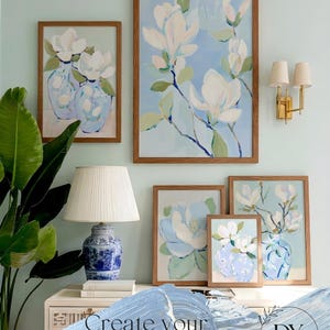 Puede incluir: Una pared de galer&iacute;a con impresiones art&iacute;sticas florales enmarcadas con flores de magnolia blancas y jarrones azules. Las obras de arte se exhiben en varios tama&ntilde;os con marcos de madera. Tambi&eacute;n se ve una l&aacute;mpara de cer&aacute;mica azul y blanca y un aplique dorado.